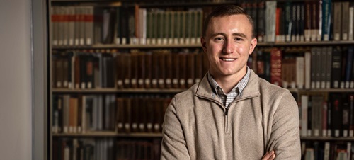 Male student standing in front of a shelf of books