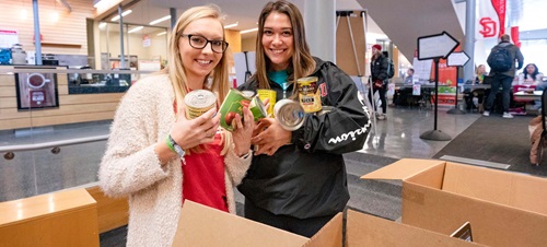 Two Female Students Helping at a Food Drive.