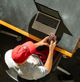 Student working on a laptop while holding a phone