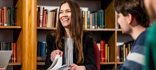 Faculty reading a book with students in library