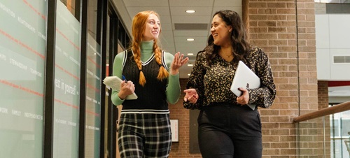 Two female students walking down a hallway in Sioux Falls, smiling and carrying books.