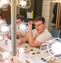Student prepares theatre makeup in front of mirror.