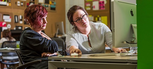 Graphic Design student works one-on-one with faculty designing in the Mac Lab
