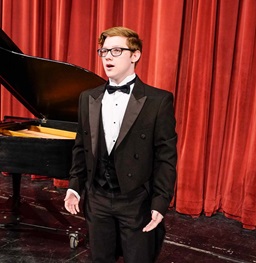 boy singing a solo on stage in front of a piano
