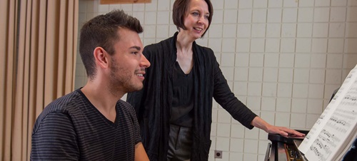 male student playing the piano with his female instructor