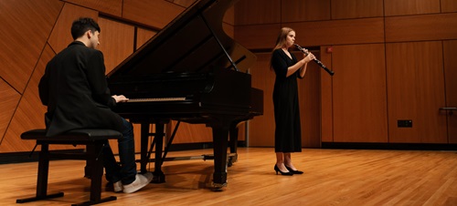 A student playing piano with another playing clarinet on stage.