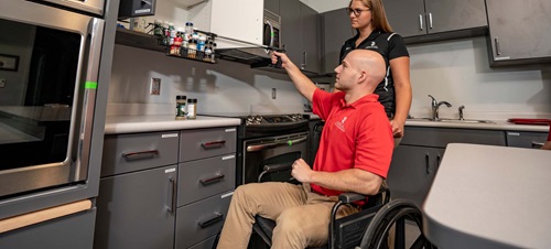 Male in a Wheelchair Using a Tool to Grab Spice from Cabinet