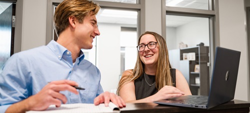 Two business students talking working on a laptop.