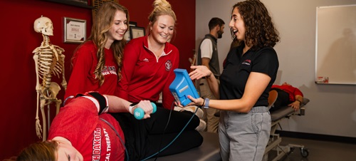 Physical therapy students analyzing a device connected to a test subject laying down on a table.