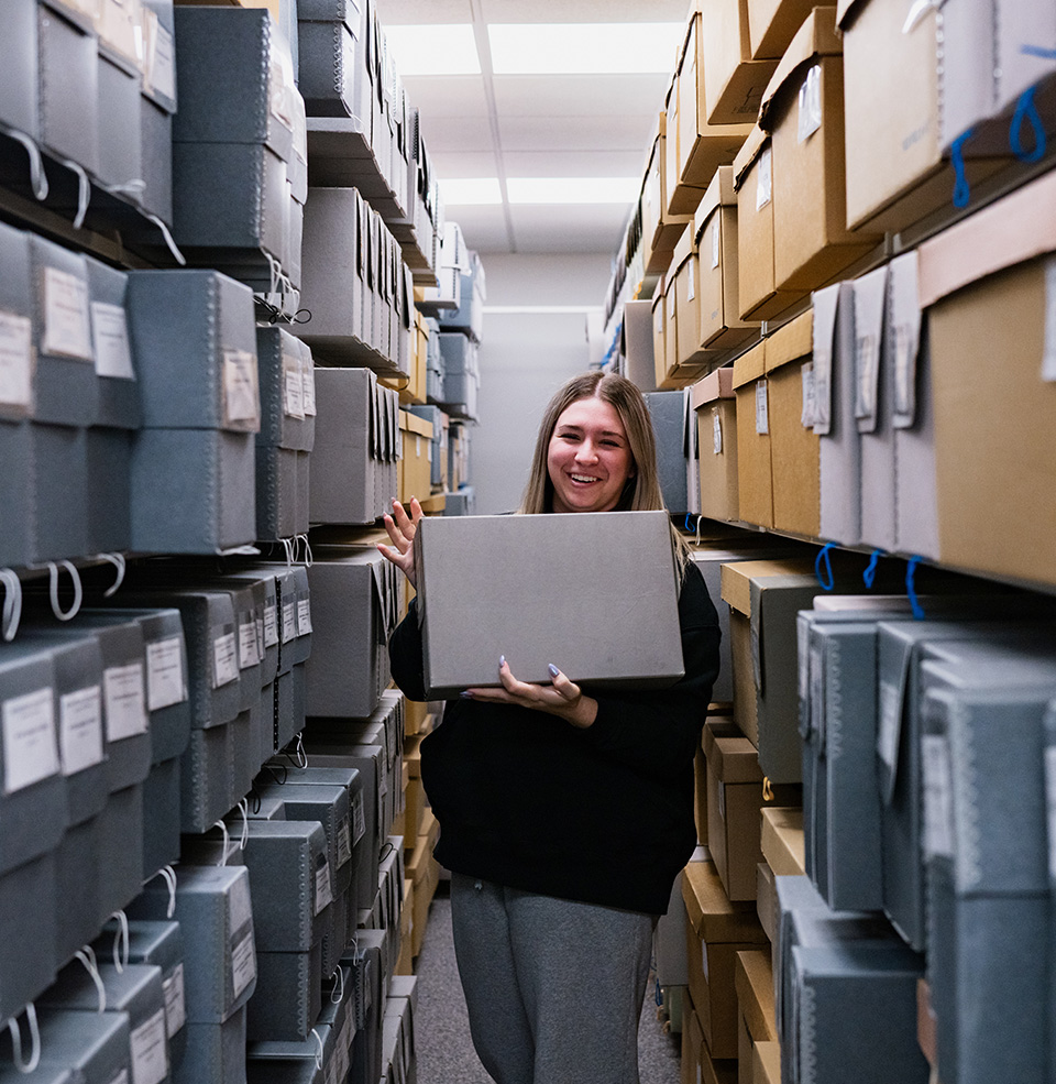 Person standing in between two shelves filled floor to ceiling with boxes of USD archives