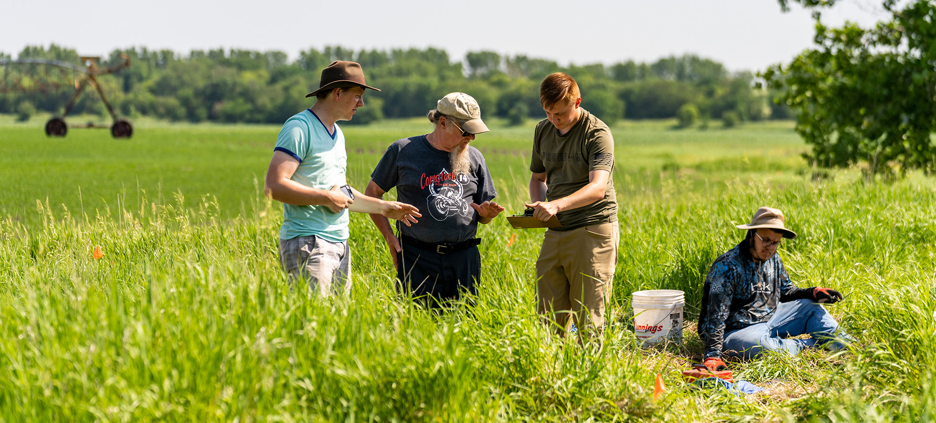 Four students in a grass prairie looking at grass and rocks 