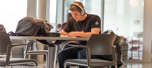 Student with headphones on sitting at a table reading a book