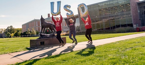Three Students Running with Balloons that Spell USD.