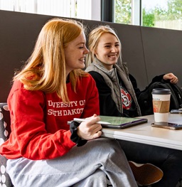 Two Females Sitting at Table Smiling