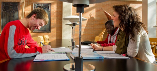 Students sitting at desk smiling and working on homework.