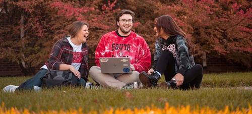 Three USD Students sitting in the grass chatting over a laptop