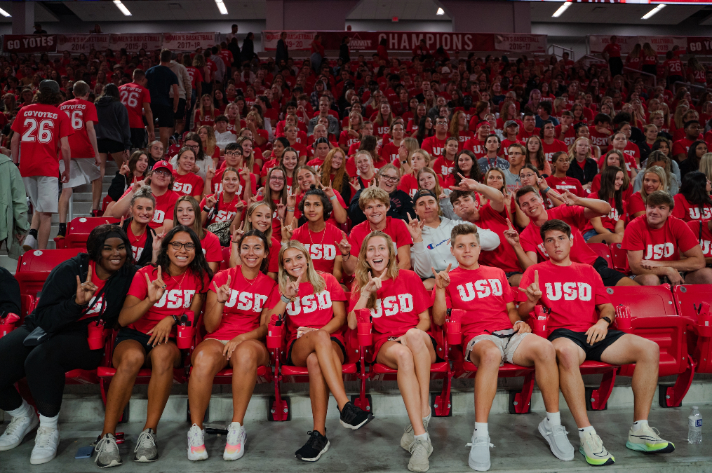 New USD undergraduate students sitting in the bleachers during move in day and smiling.