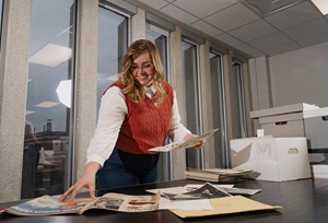 A journalism student smiling while researching old newspaper clippings.