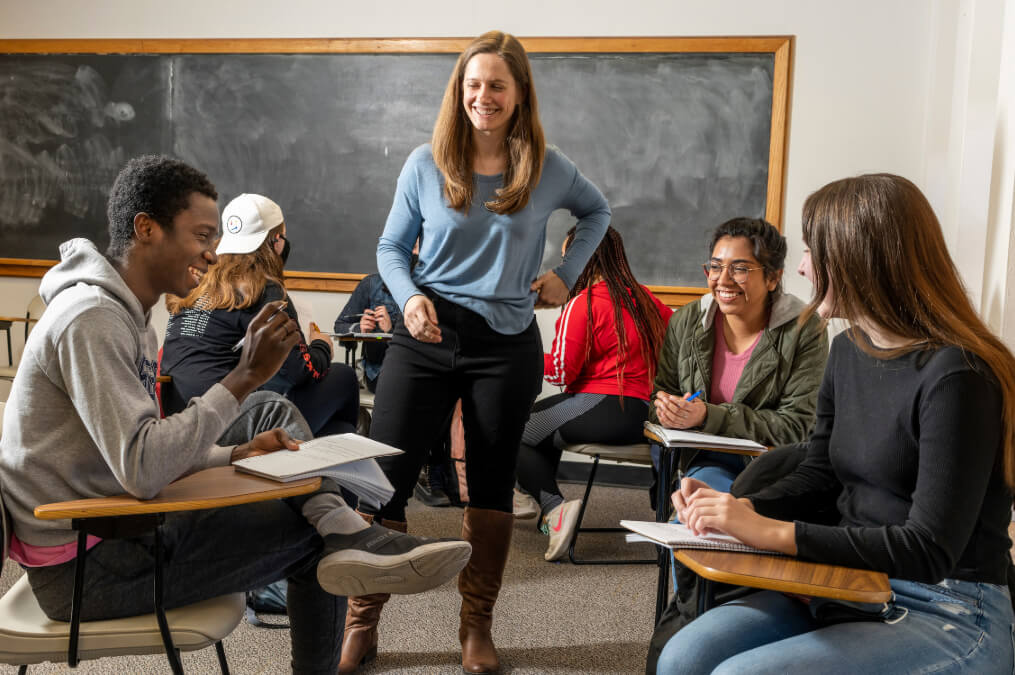 A sociology class in progress with a teacher circled by students sitting in desks.