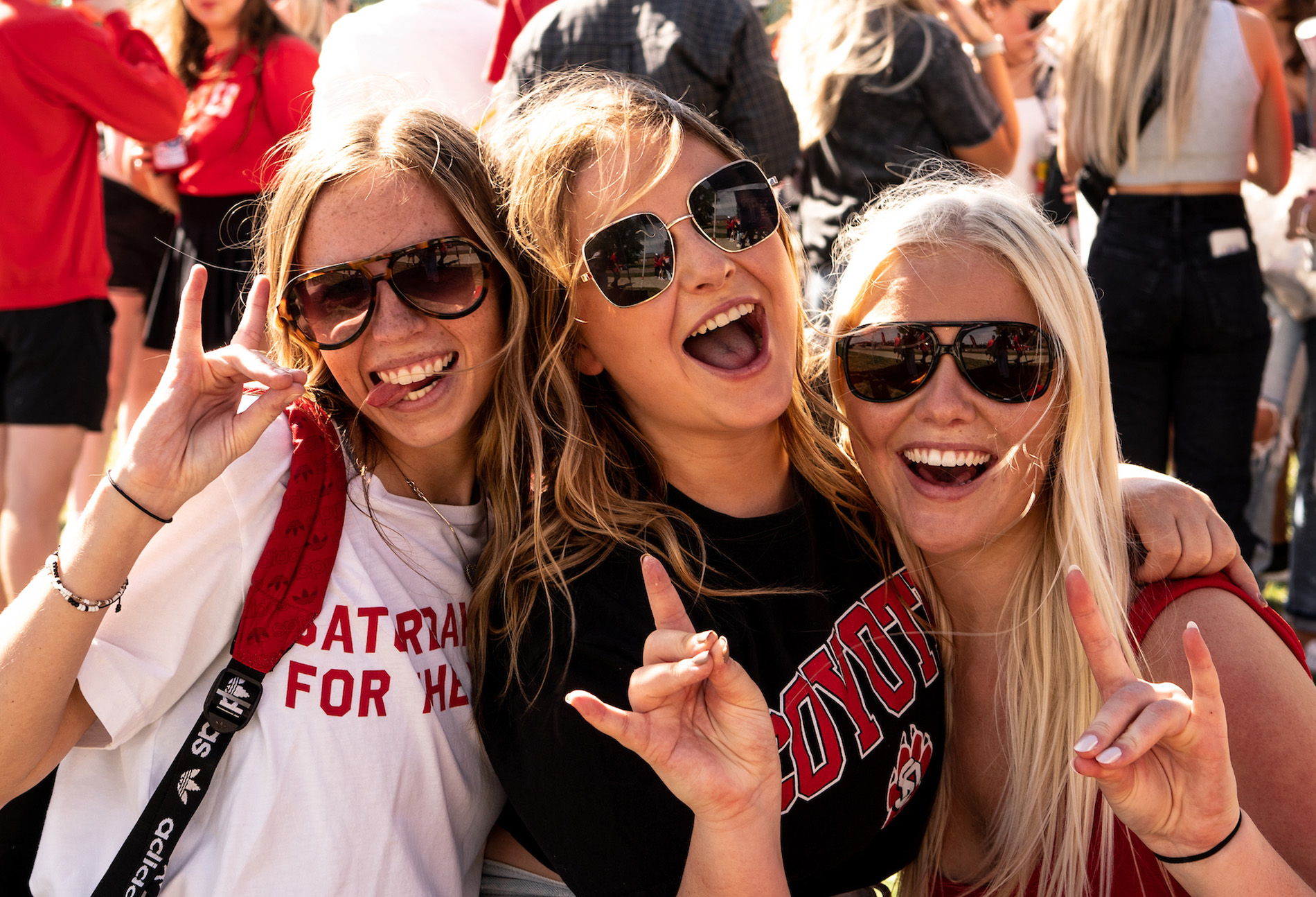 Three girls in USD shirts smiling and holding up a hand Yote sign.