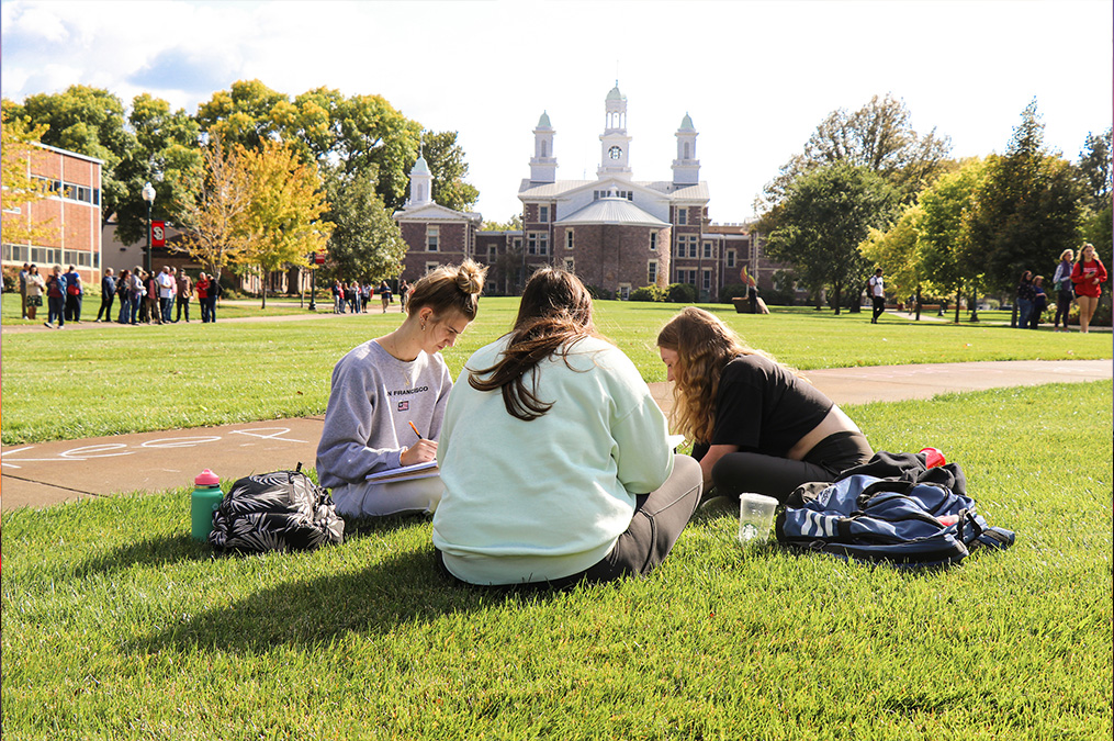 Three female students studying on the MUC lawn during the day.
