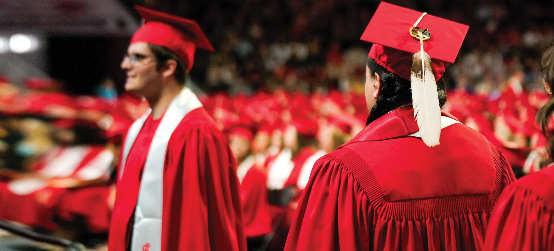 Native American student in red gown and mortarboard cap with feather at commencement