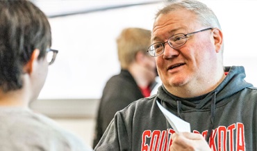 A teacher assisting a student while both are smiling in a classroom.
