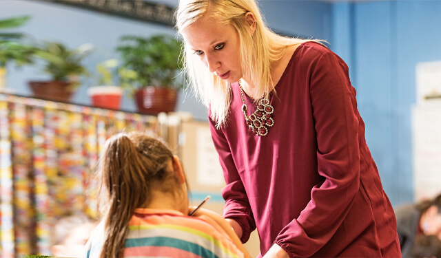A teacher assisting a young student in a classroom.