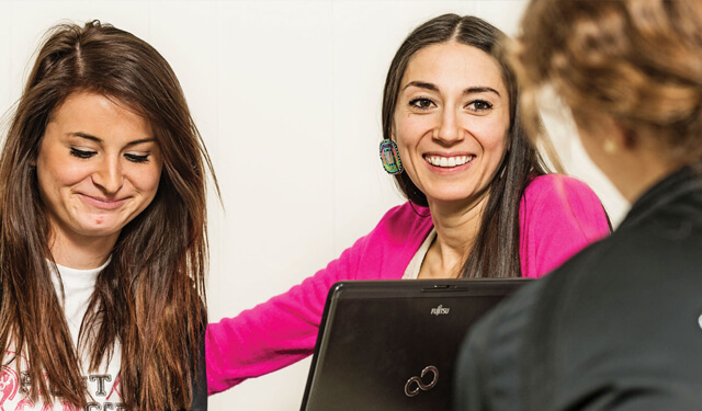 A teacher assisting a student while both are smiling in a classroom.
