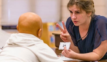 A teacher assisting a young student while she is holding up two fingers.