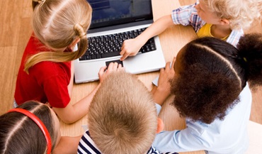 Young students sitting around a laptop watching a video.
