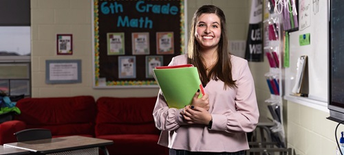 A student teaching holding her folders and notes smiling in a classroom.