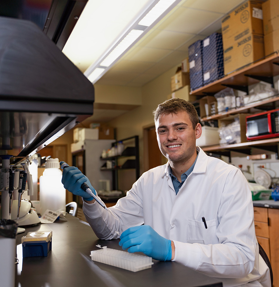 Student holding a dropper in a white lab coat and gloves