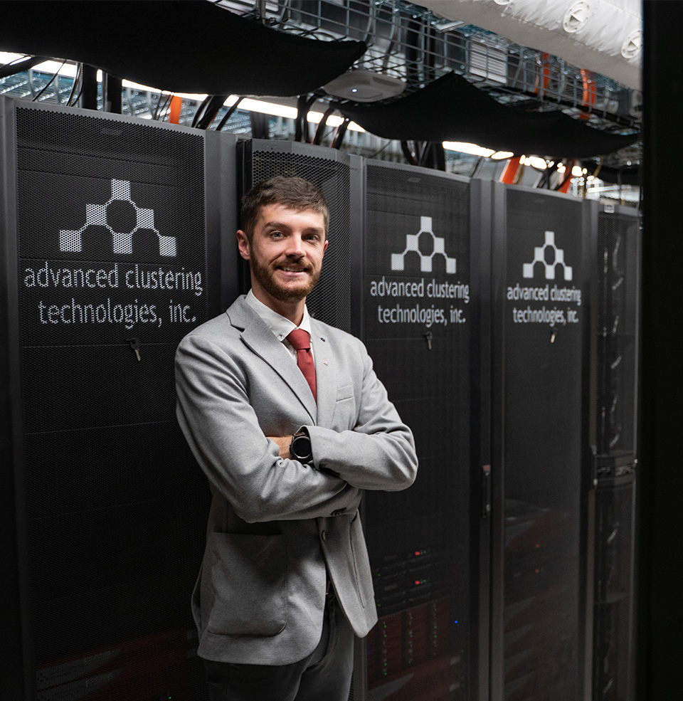 Student standing in nice jacket with arms crossed in front of computer servers and wires