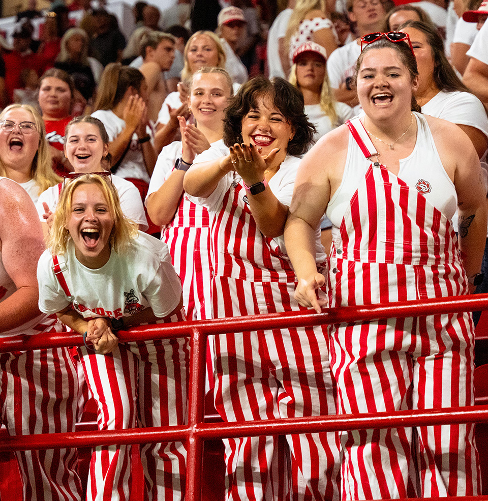Coyote Crazy students in red and white striped pants cheer for the USD Football team.