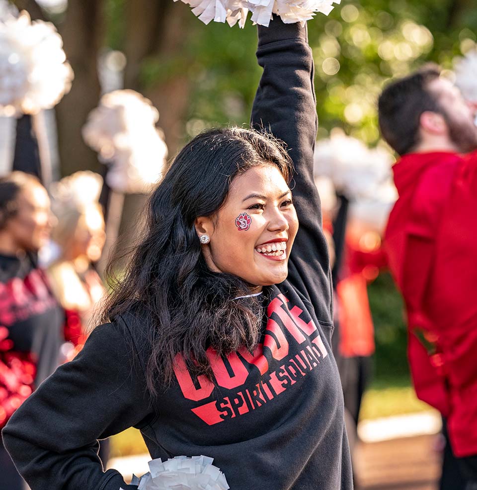 A USD Spirit Squad Member smiling and cheering with poms.