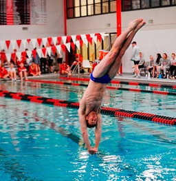 A USD male swimmer diving into the pool.