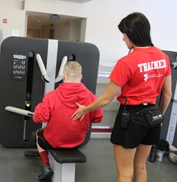 A USD Wellness Center trainer helping a personal with a lifting machine.