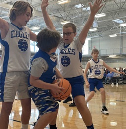 A youth team playing basketball on a wellness center court as a child goes up for a shot.