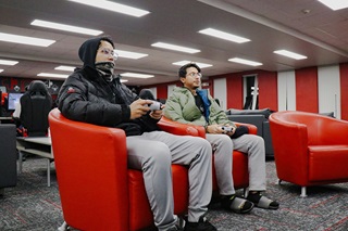 Two students playing a console game in the esports arena red chairs.