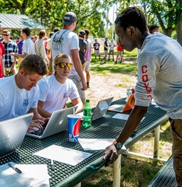 A Fraternity recruiting table with two men on laptops talking to a potential recruit.