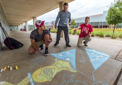 Fraternity students posing in front of their logo.