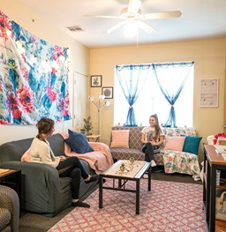 Two female students sitting in a dorm room talking.