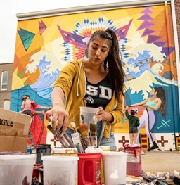 A USD student mixing colors to paint on the wall mural in downtown Vermillion.