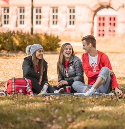 Three USD students sitting and laughing on the campus lawn.