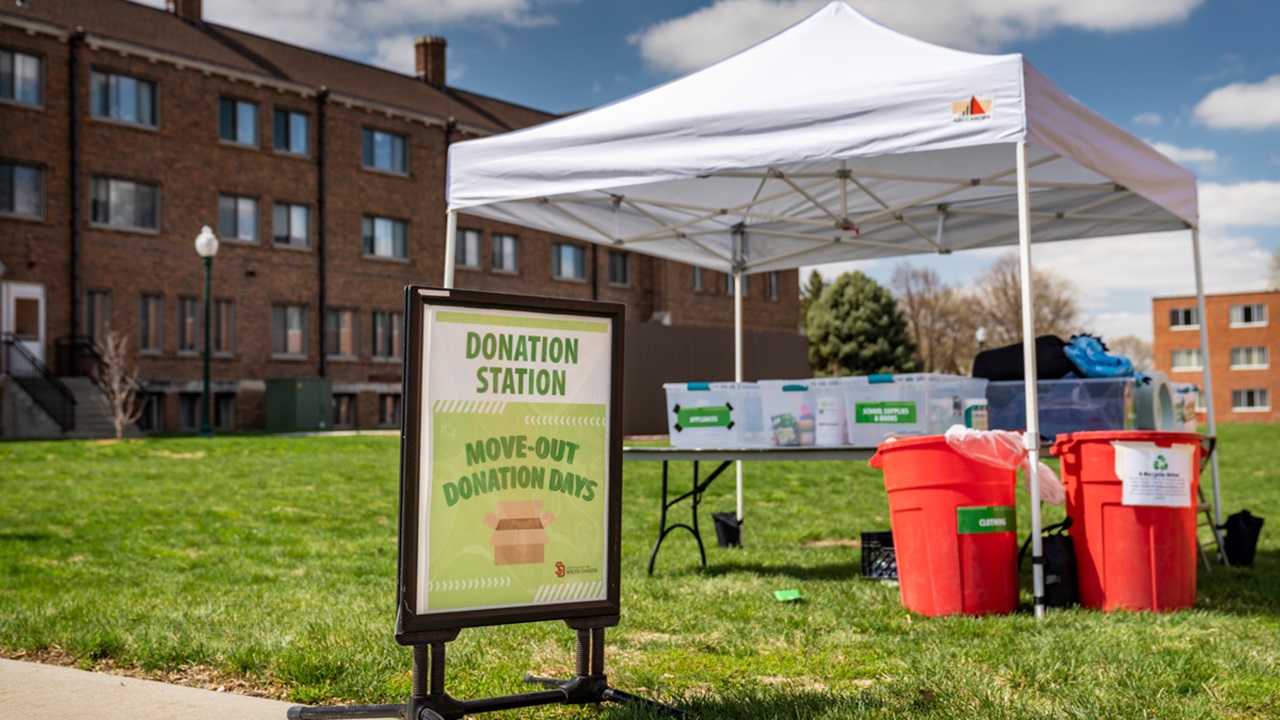 A picture of a donation sign and a tent with a table underneath to collect items.