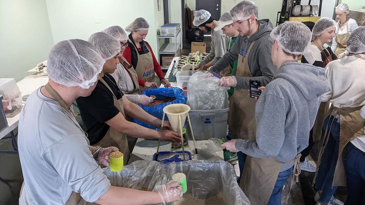 Beta Alpha Psi members stand around a table and package meals.