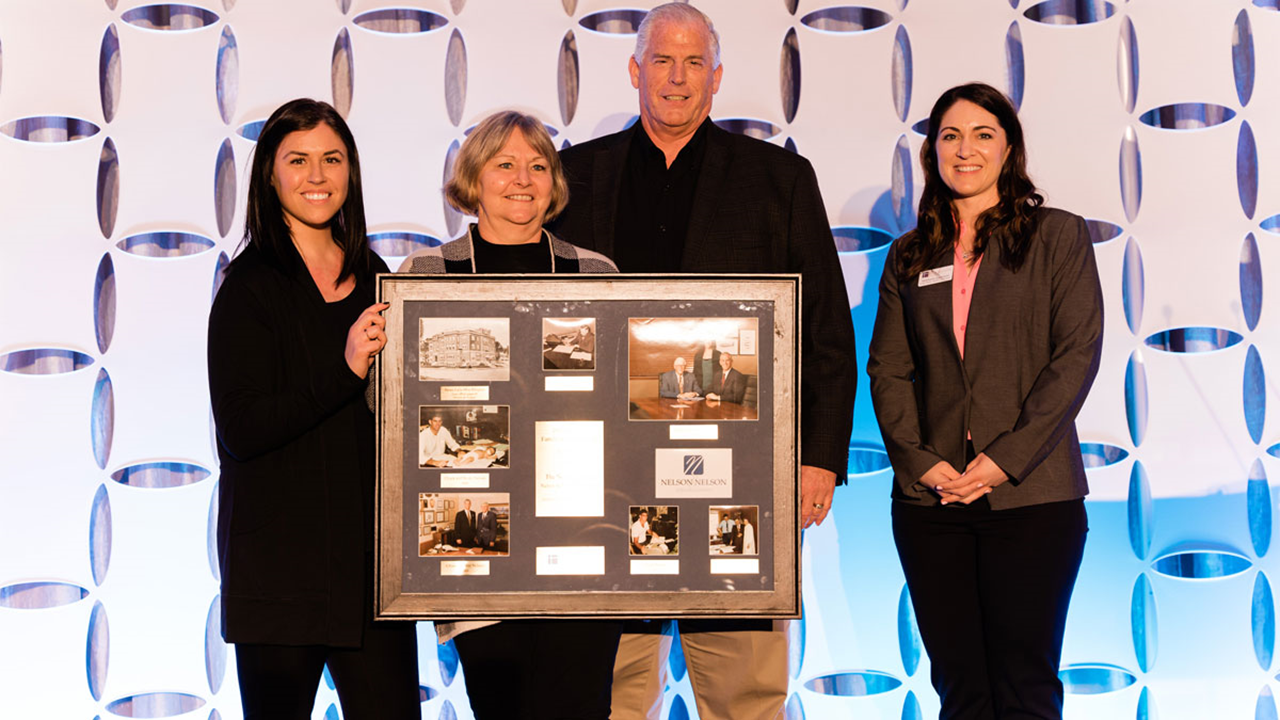 Four people stand on a stage and hold up a frame filled with pictures and letters.