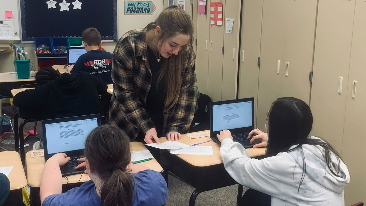 Alisa Larsen leans over a desk and helps a student in the classroom.