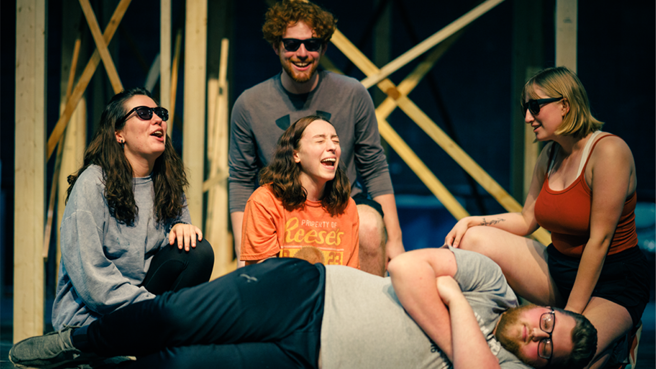 Five students sing and crowd around each other on stage.